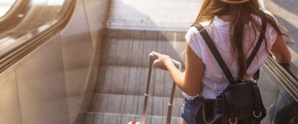 Young,Girl,With,Suitcase,Down,The,Escalator.